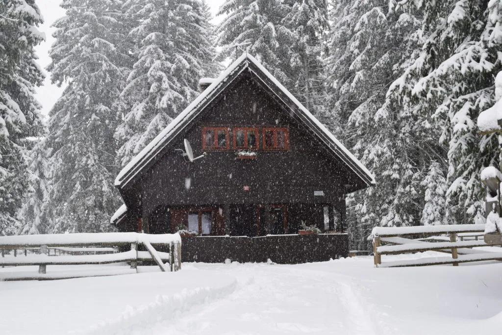 Koča Chalet Pokljuka med sneženjem, obdana z zasneženimi smrekami